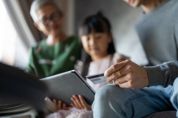 A child watching a parent pay online with a card while a grandparent looks on